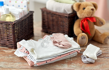 婴儿期服装婴儿服装,泰迪熊玩具篮子木制桌子家里婴儿衣服泰迪熊玩具放家里的桌子上图片