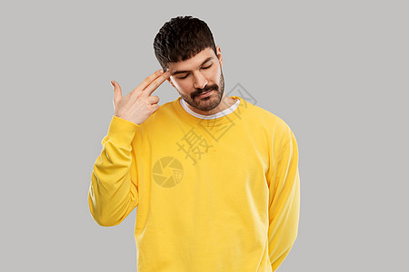 人,表情压力的无聊的年轻人穿着黄色运动衫,用手指的手势头部射击无聊的人做手指的手势图片