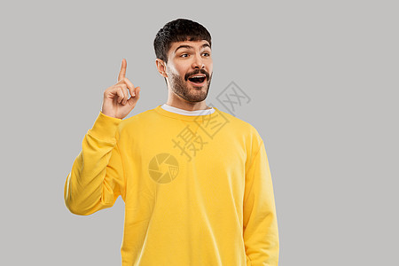 伯爵人们的微笑的年轻人穿着黄色运动衫,灰色背景上根手指年轻人穿着黄色运动衫展示根手指图片