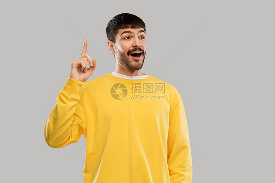 伯爵人们的微笑的年轻人穿着黄色运动衫,灰色背景上根手指年轻人穿着黄色运动衫展示根手指图片