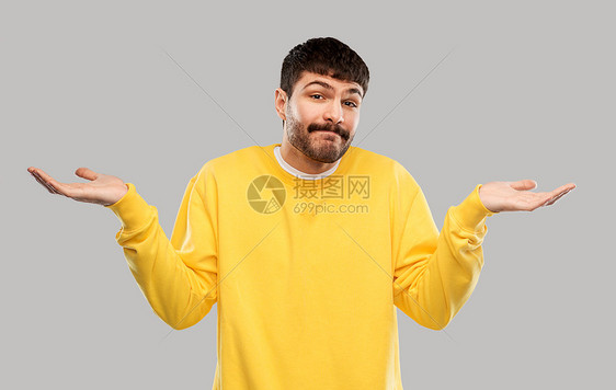 人,情感表达困惑的人穿着黄色运动衫灰色背景上耸耸肩穿着黄色运动衫的困惑的人耸耸肩图片