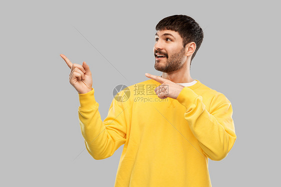 人们的微笑的年轻人穿着黄色运动衫,指着灰色背景上的东西微笑的人指着什么东西图片