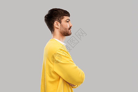 人们的年轻人穿着黄色运动衫,双臂交叉灰色背景上穿着黄色运动衫的年轻人交叉手臂图片