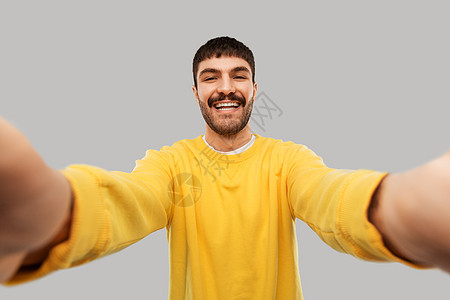 人们的快乐微笑的年轻人穿着黄色运动衫,灰色背景下自拍穿着黄色运动衫自拍的快乐年轻人图片