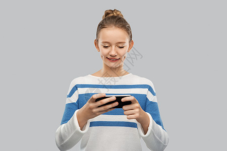 技术人的快乐的微笑少女套衫用智能手机灰色背景快乐微笑的十几岁女孩用智能手机图片
