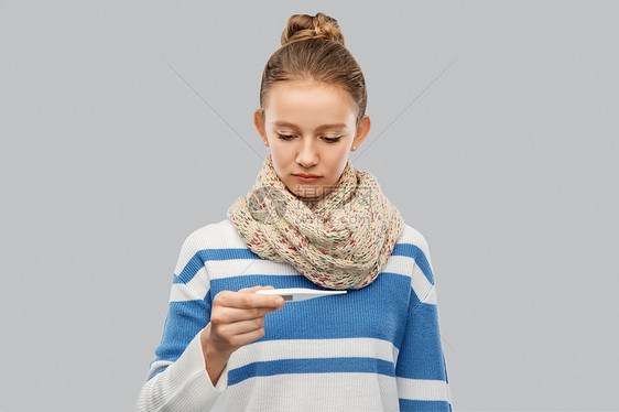 人,健康问题发烧悲伤的病少女围巾测量温度温度计灰色背景戴围巾测量温度的生病少女图片