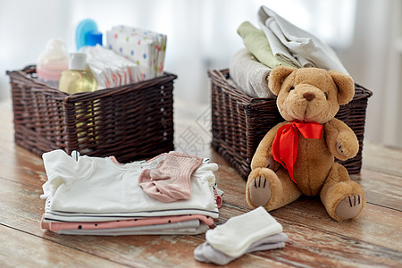 婴儿期服装婴儿服装,泰迪熊玩具柳条篮子木制桌子家里婴儿衣服泰迪熊玩具放家里的桌子上图片
