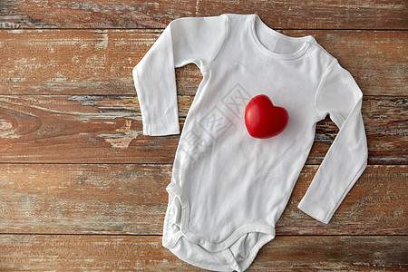 婴儿服装,婴儿期服装紧身衣与红色心脏玩具木制桌子上婴儿紧身衣,木制桌子上有红色的心脏玩具图片