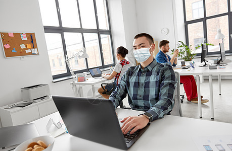 健康安全大流行创造的人戴着保护医疗面罩,办公室工作时用笔记本电脑防止病戴着医用面具的男人办公室工作,带图片