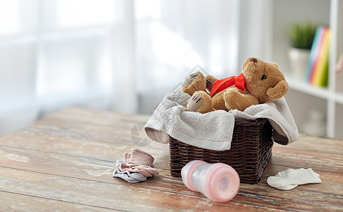 婴儿期服装泰迪熊玩具柳条篮子与婴儿的东西木制桌子家里泰迪熊玩具篮子里,婴儿的东西桌子上图片