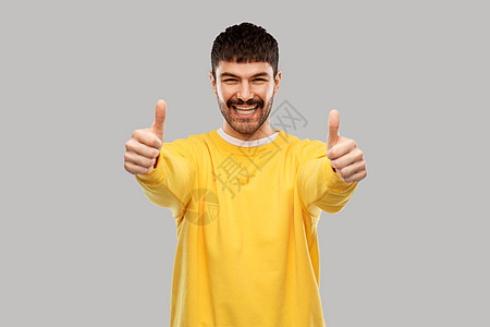 手势人们的微笑的年轻人穿着黄色运动衫,灰色的背景上竖起大拇指微笑的年轻人竖起大拇指图片