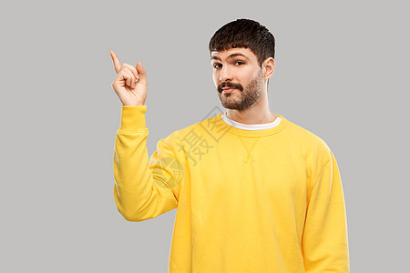 人们的穿着黄色运动衫的年轻人指着灰色背景上的东西指指点点的人图片
