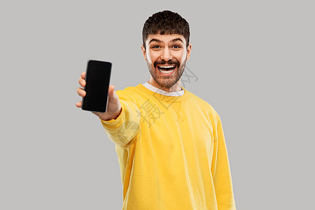 技术,沟通人的快乐的微笑年轻人展示智能手机灰色背景快乐微笑的年轻人展示智能手机图片