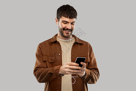音乐,技术人的微笑的年轻人与耳机智能手机灰色背景带着耳机智能手机的微笑的年轻人图片