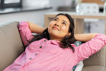 人与休闲的快乐的亚洲年轻女人穿着粉红色的衬衫躺沙发上,家做梦亚洲女人躺沙发上,家做梦图片