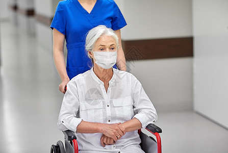 医学,健康安全大流行护士携带老年妇女病人轮椅上佩戴面部防护医疗面罩,以防止病疾病医院走廊医院里戴着轮椅面具的图片