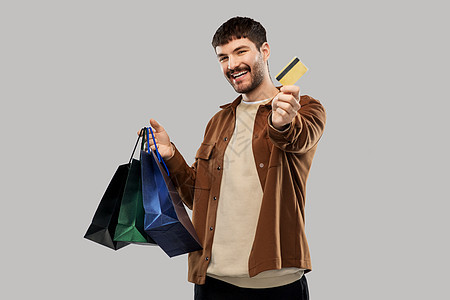 销售人们的快乐的微笑年轻人与购物袋信用卡灰色背景带着购物袋信用卡的快乐年轻人图片