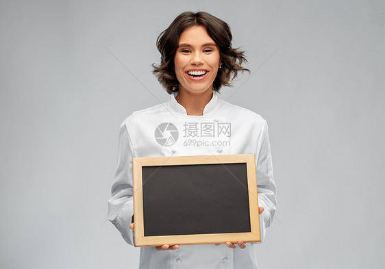 烹饪,广告人的快乐微笑的女厨师着黑色黑板灰色的背景微笑的女厨师着黑色黑板图片