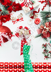 女手穿绿色圆点上衣,白色桌面上用各种红色节日装饰丝带包装纸制作节日圣诞时髦的蝴蝶结上面的风景平躺图片