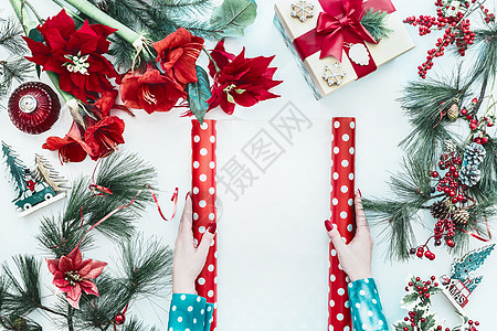 女手穿着蓝色衬衫,着红色圆点包装纸,白色桌子上有,上面有圣诞花礼品盒冷杉树枝,顶部有风景平躺图片