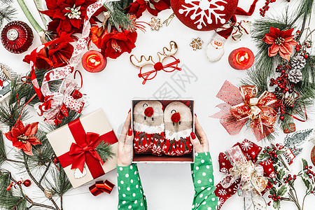女手穿着绿色衬衫,着打开的礼品盒,白色背景上有滑稽的鹿袜,红色的圣诞装饰有冷杉枝蜡烛上面的风景平躺图片