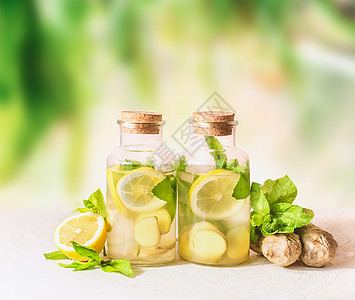 健康的夏季柠檬水饮料白色桌子上的绿色阳光自然背景生姜,柠檬,薄荷叶柠檬水注入水图片