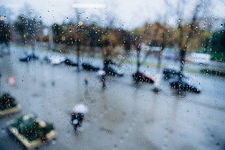 人们走街上的雨中,透过潮湿的窗户观看图片