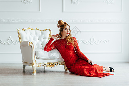 年轻的女孩,红色的头发,穿着件鲜红色的连衣裙,间古色古香的沙发上的明亮的房间里图片