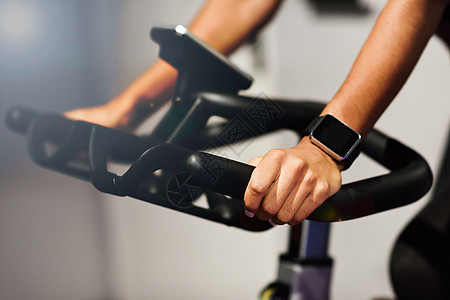 晨骑自行车手女人戴着智能手表在健身房锻炼背景