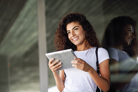 快乐的年轻阿拉伯妇女商业背景中用数字平板电脑快乐的女孩穿着运动服,微笑着微笑的阿拉伯女孩商业背景中用数字平板电脑图片