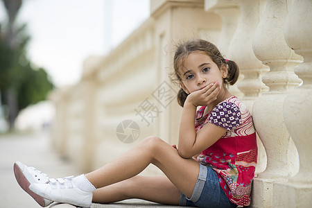 可爱的小女孩梳着辫子,坐户外的城市地板上可爱的小女孩梳着辫子图片