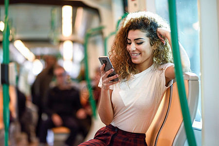 地铁里的年轻阿拉伯女人看着她的智能手机穿着休闲服的女地铁里的阿拉伯女人看着她的智能手机背景图片