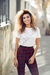 美丽的年轻阿拉伯女人,黑色卷发街上穿便装的阿拉伯女孩快乐的女穿着白色T恤检查裤街上穿着休闲服的阿拉伯女孩图片