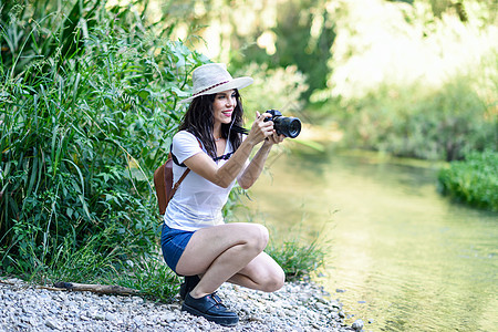 美丽的徒步旅行者年轻女人用无镜相机拍照,戴着草帽,乡下徒步旅行徒步旅行者女人用无镜相机拍照图片