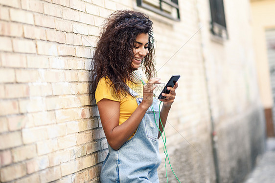 年轻的北非女人户外用她的智能手机发短信微笑的阿拉伯女孩穿着休闲服装,黑色卷发年轻的北非女人户外用她的智能手机发短信图片