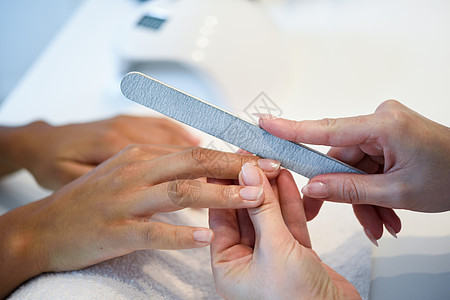 美甲沙龙接受美容师修指甲的女人的特写美容师给顾客留指甲指甲沙龙里的女人用指甲锉修指甲图片