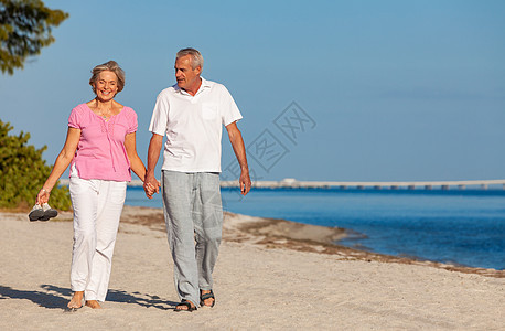 幸福的老年男女夫妇个荒凉的热带海滩上散步,笑着牵手度假,那里有明亮的蓝天平静的大海图片