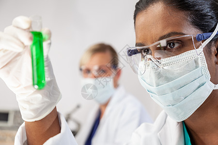 亚洲女医学或科学研究人员或医生实验室或实验室里看着绿色溶液的试管,她的女同事她身后注意力集中图片