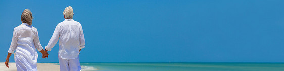帕诺拉后视幸福成功的退休老年男女夫妇步行牵手个荒芜的热带海滩上,明亮的蓝天全景网络横幅图片
