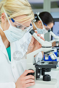 女医学或科学研究者科学家或医生实验室用显微镜,她的同事她身后注意力集中图片