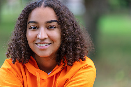 户外肖像美丽的快乐混合种族,混血非裔美国女孩,十几岁的女青年,微笑着,有着完美的牙齿,穿着橙色的帽衫图片