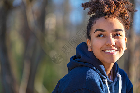 户外肖像美丽的快乐混合种族,混血非裔美国女孩,十几岁的女青年,微笑着,完美的牙齿,穿着蓝色的帽衫图片