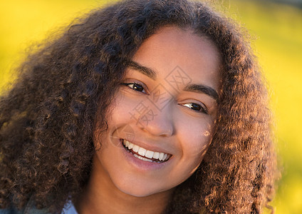 户外肖像美丽的快乐混合种族非裔美国女孩十几岁的女年轻女子微笑与完美的牙齿户外草地黄花图片