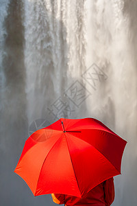 穿着红色外套夹克的轻女子,瀑布前着把红色的伞图片
