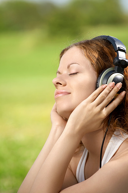 美丽的女孩公园的耳机里听音乐的肖像