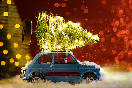圣诞老人穿着蓝色复古玩具车,节日背景上送圣诞或新年照明树圣诞老人送圣诞或新年树图片