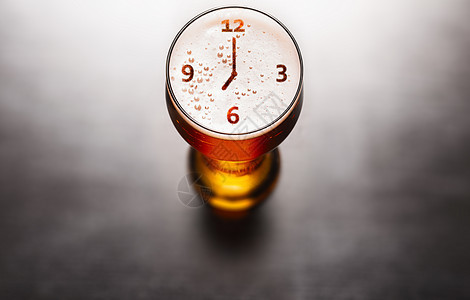 啤酒的时间到了黑色桌子上啤酒玻璃泡沫上的时钟或手表符号,上面看啤酒的时间到了图片