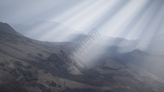 太阳的光线山脉的背景下,前景的熔岩岩石潮湿的海岸上阳光照射群山的背景上图片