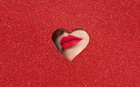 个年轻漂亮的女人用红色口红的美丽丰满明亮的嘴唇,看着由彩色纸制成的心形图案假日模式情人节美丽的爱情化妆背景图片