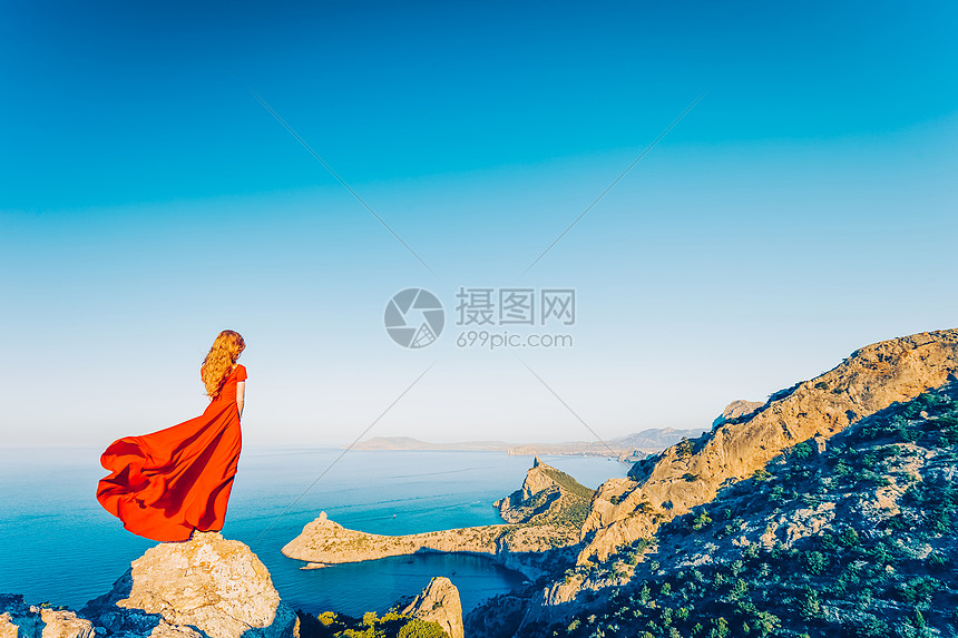 穿着红色连衣裙的年轻美女望着山海蓝天背景上的自然女孩时尚照片图片
